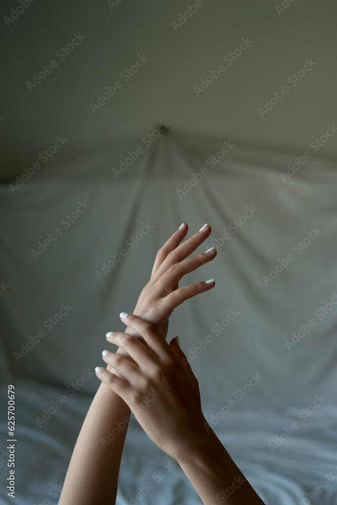 close up of woman hands and arms crossed on bed sheet with delicate soft natural light. Concept of hand care and manicure. natural nails. vertical