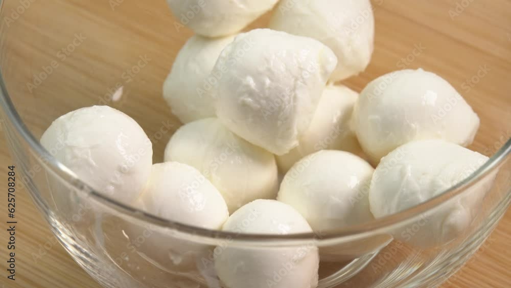 Mozzarella balls cheese are rotate into a glass bowl. Ingredients for making pizza or fresh tomato salad Mozzarella balls cheese are rotate into a glass bowl. Ingredients for making pizza or fresh tomato salad