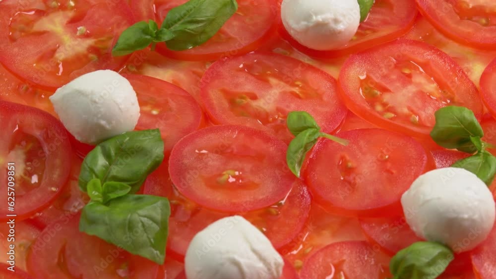 Sliced fresh tomatoes with fresh basil leaves and mozzarella balls for tomato carpaccio rotate as background. Preparations for pizza or vegetable salad. Tomato slices close up