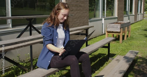 Happy student sitting on bleachers while studying in front of a school