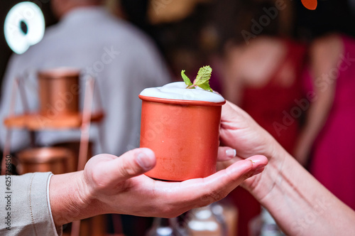 Photography A copper cup with a moscow mule being handed by one hand to another hand