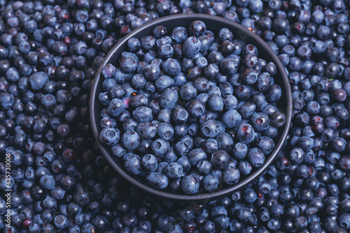 Fresh blueberries in black bowl on blueberries background.  Close-up. Top view. Bowl filled with ripe blueberries.