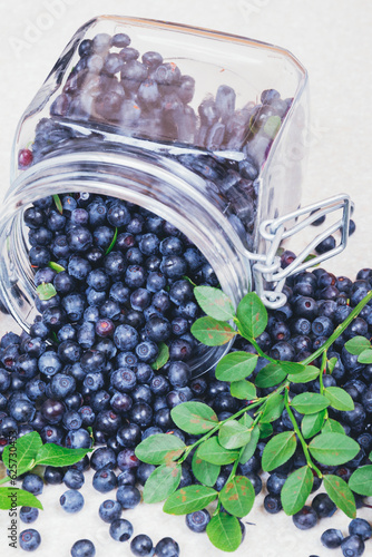 Scattered blueberry from the glass jar on a light table.Glass jar filled with ripe blueberries. 