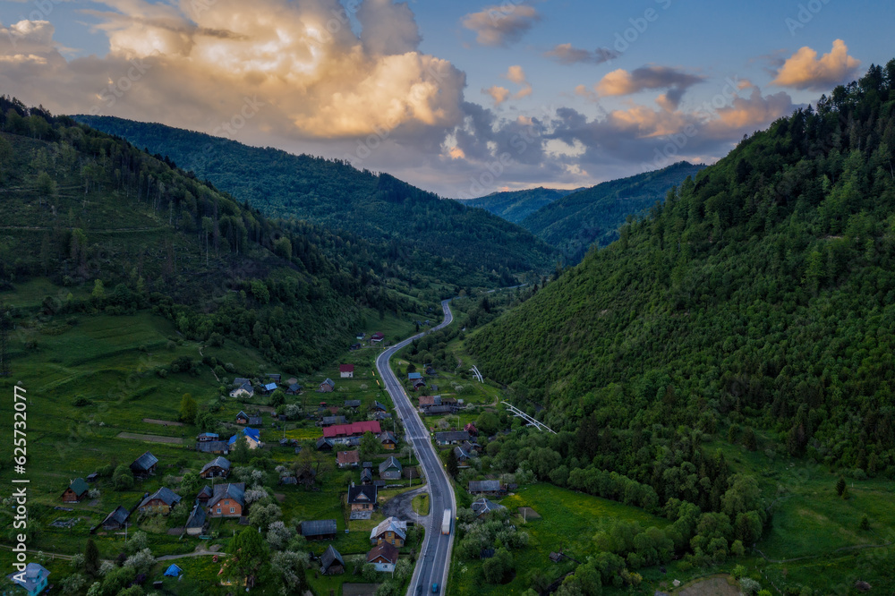 Beautiful landscape from a height. Typical Carpathian village in a valley, forest and mountains under blue sky with white clouds. Kozyova, Carpathians, Ukraine. Aerial drone shot