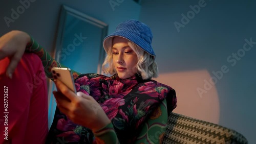 Fashionable young woman sitting on the sofa, surfing a on the internet on her mobile phone