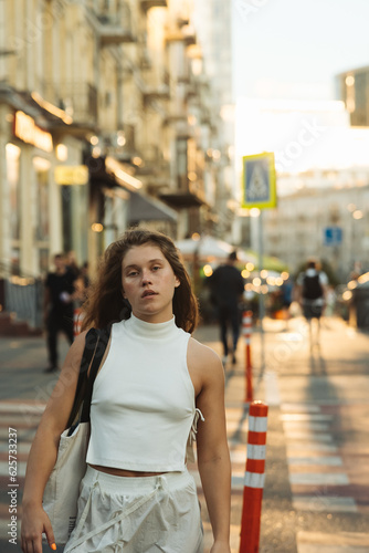 A stylish girl in white clothing with curly hair on the morning city streets.