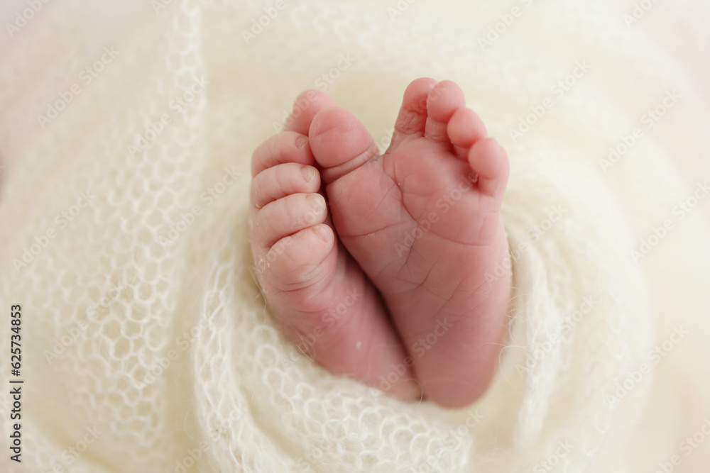 The tiny foot of a newborn baby. Soft feet of a new born in a white wool blanket. Close up of toes, heels and feet of a newborn. Knitted white heart in the legs of a baby. Macro photography. The tiny foot of a newborn baby. Soft feet of a new born in a white wool blanket. Close up of toes, heels and feet of a newborn. Knitted white heart in the legs of a baby. Macro photography.