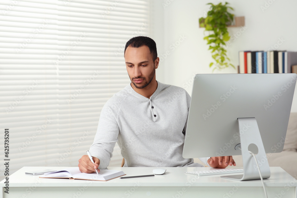 Young man working on computer at desk in room. Home office Young man working on computer at desk in room. Home office