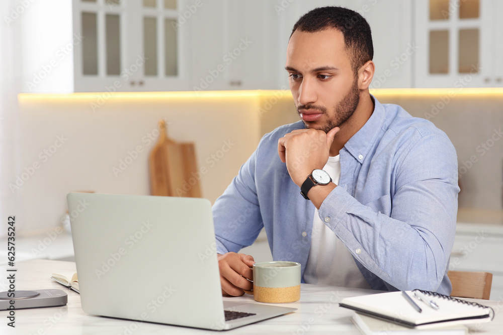 Young man working on laptop at desk in kitchen. Home office Young man working on laptop at desk in kitchen. Home office