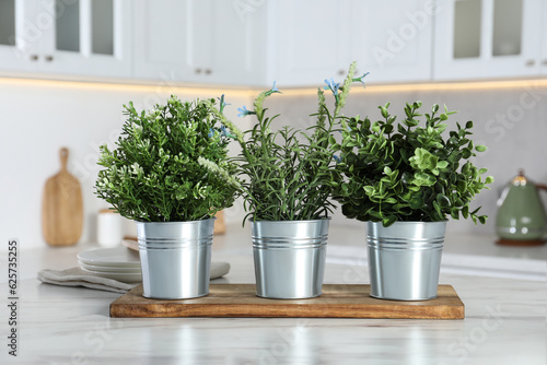 Different artificial potted herbs on white marble table in kitchen