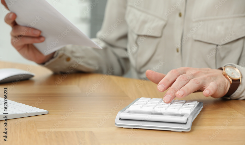 Fototapeta premium Professional accountant using calculator at wooden desk in office, closeup