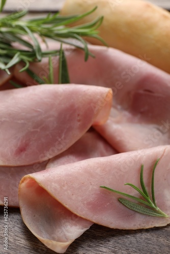 Slices of delicious ham and rosemary on wooden table, closeup