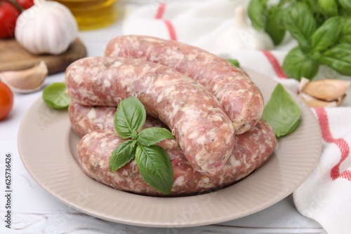 Raw homemade sausages and basil leaves on white table, closeup