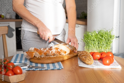 Pregnant young woman cuts bread into slices for sandwiches