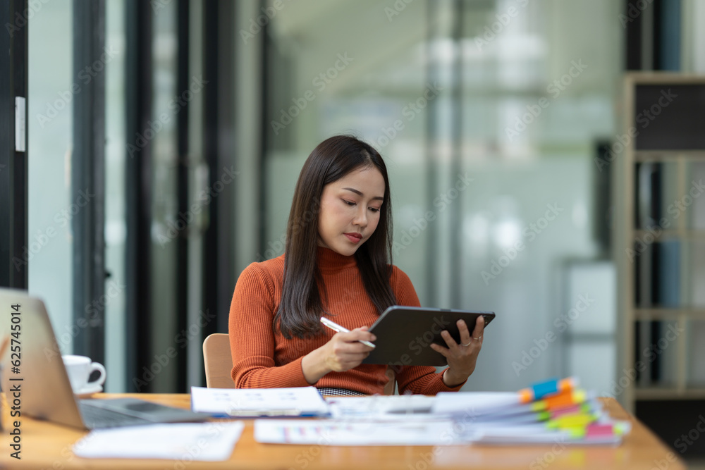 Asian businesswoman using tablet, laptop at modern office to research, record, to make account analysis report, real estate investment data. Division of paperwork. Finance and tax system concept.