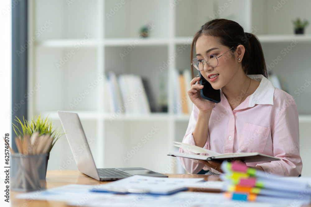Confident Asian businesswoman using mobile phone to contact customers to talk Negotiate on business matters Happily logging deals while sitting at his desk in the office. Confident Asian businesswoman using mobile phone to contact customers to talk Negotiate on business matters Happily logging deals while sitting at his desk in the office.