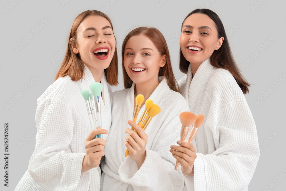 Young women with makeup brushes on grey background Young women with makeup brushes on grey background