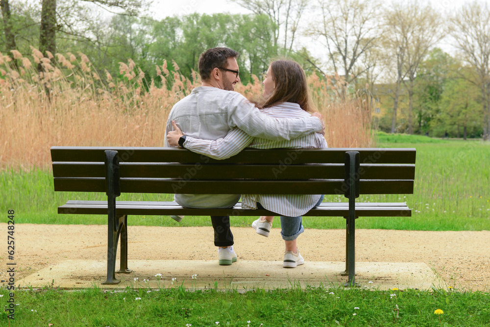 Beautiful loving couple sitting on bench and hugging in park Beautiful loving couple sitting on bench and hugging in park