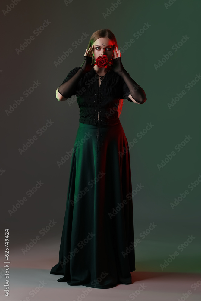 Beautiful young witch with flower on dark background