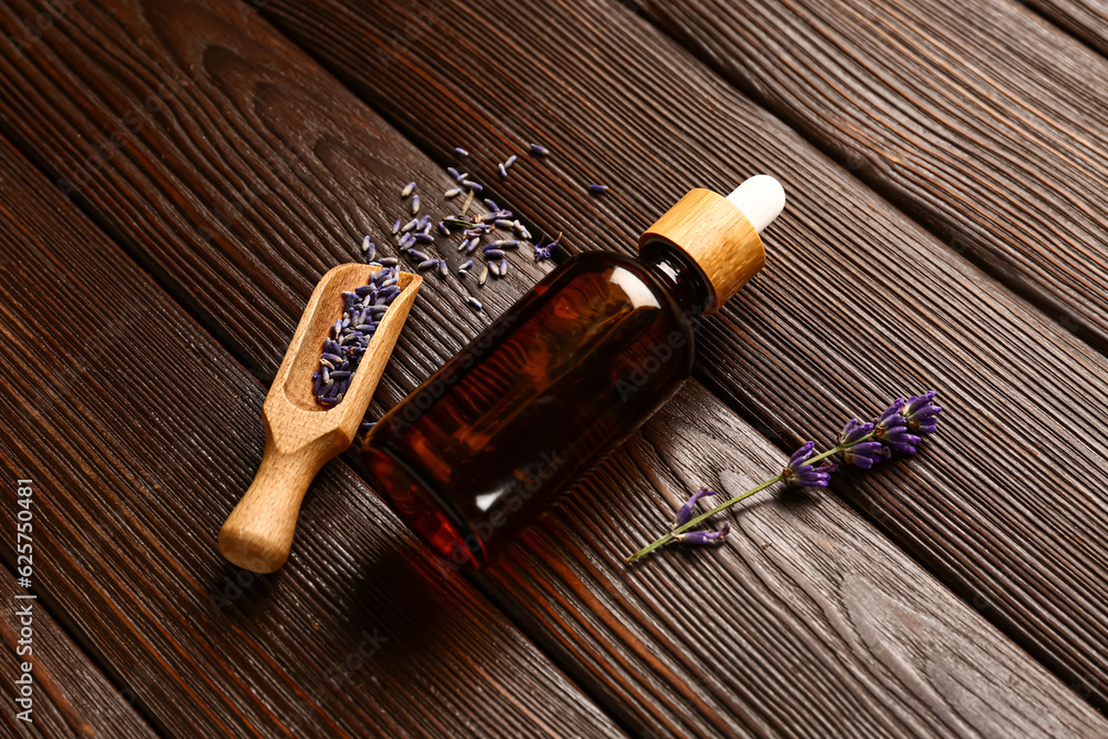 Bottle of essential oil and lavender flowers on dark wooden background