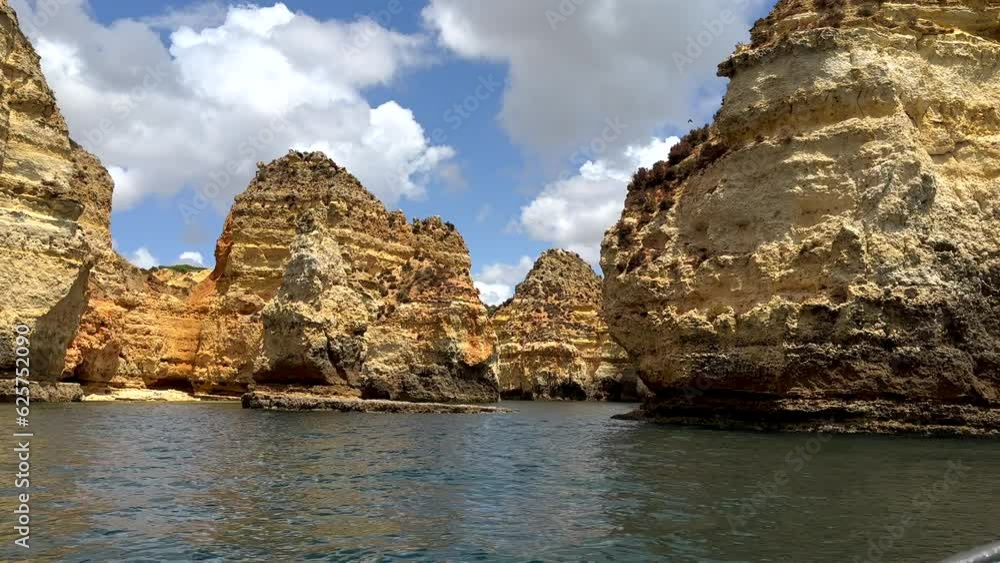 Wide shot showing stunning sandstone cliff formation of algarve during boat trip on atlantic - puffy clouds at sky in background Wide shot showing stunning sandstone cliff formation of algarve during boat trip on atlantic - puffy clouds at sky in background