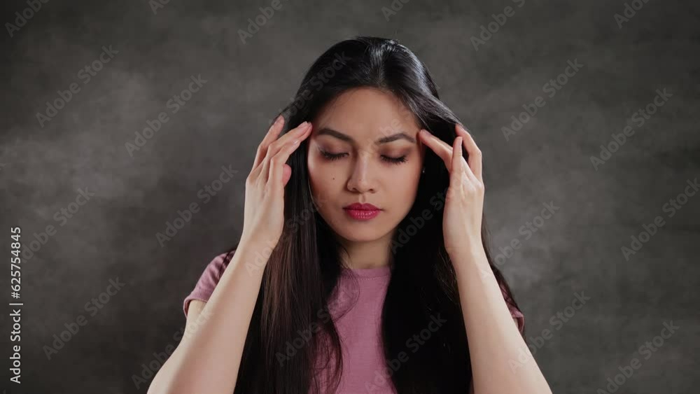 Young Asian woman in a studio has a terrible headache - extreme slow motion Young Asian woman in a studio has a terrible headache - extreme slow motion