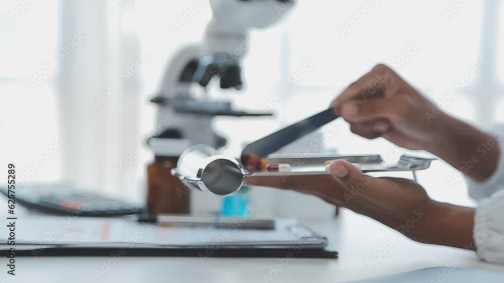 Medical worker in lab coat and sterile mask, doing a microscope analysis while her colleague are working behind Medical worker in lab coat and sterile mask, doing a microscope analysis while her colleague are working behind