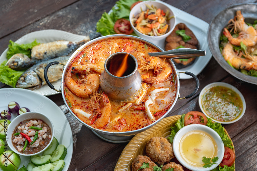 Tom Yam Kung or Tom Yum soup is Thai hot spicy soup shrimp or prawn with lemon grass, lemon, galangal, mushrooms, coconut milk and chili in bowl on wooden table top view, famous Thai food cuisine.