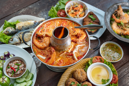 Tom Yam Kung or Tom Yum soup is Thai hot spicy soup shrimp or prawn with lemon grass  lemon  galangal  mushrooms  coconut milk and chili in bowl on wooden table top view  famous Thai food cuisine.