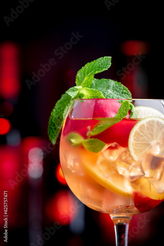 Rose sangria summer alcoholic drink with pink wine, peach, orange, lime and ice. Black bar counter background, steel bar tools and bottles