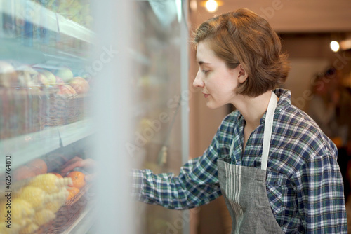 Happy female shopkeeper arranging or preparing a fruits and vegetables on a shelf in supermarket. Female supermarket staff preparing food and vegetable on a shelf.