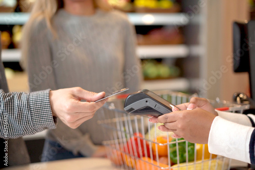 Customer using wireless digital payment on smartphone and credit card at the supermarket or grocery store.