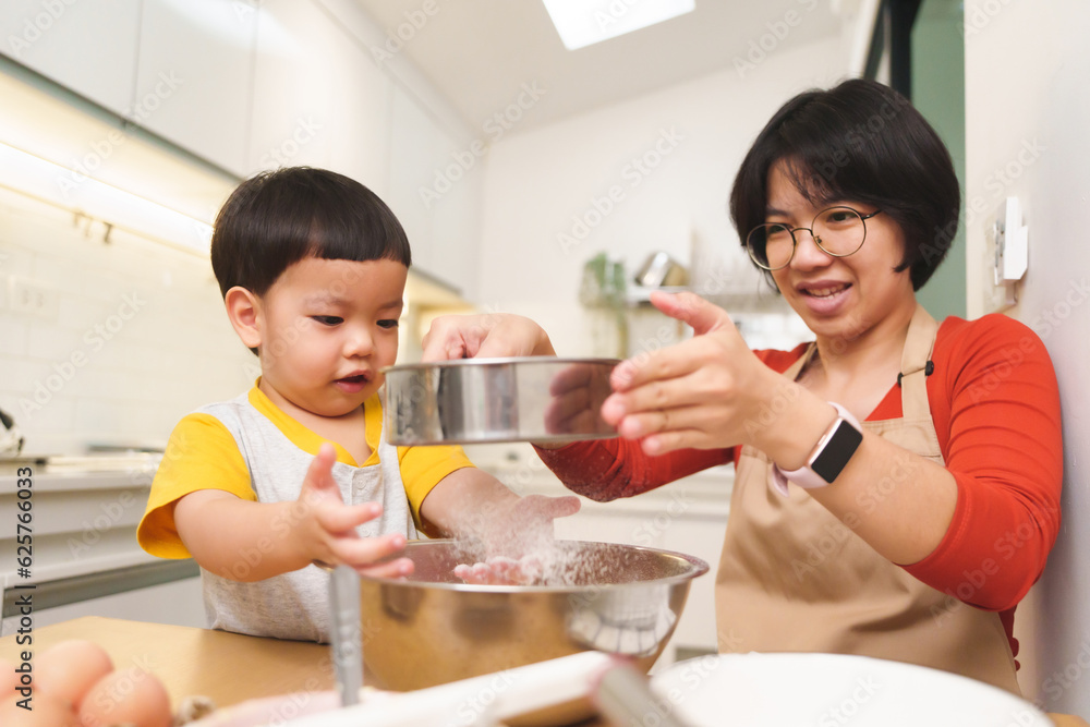 Asian Mother and her Little boy sifting flour into a bowl while baking pastry in kitchen. Cooking Asian Mother and her Little boy sifting flour into a bowl while baking pastry in kitchen. Cooking