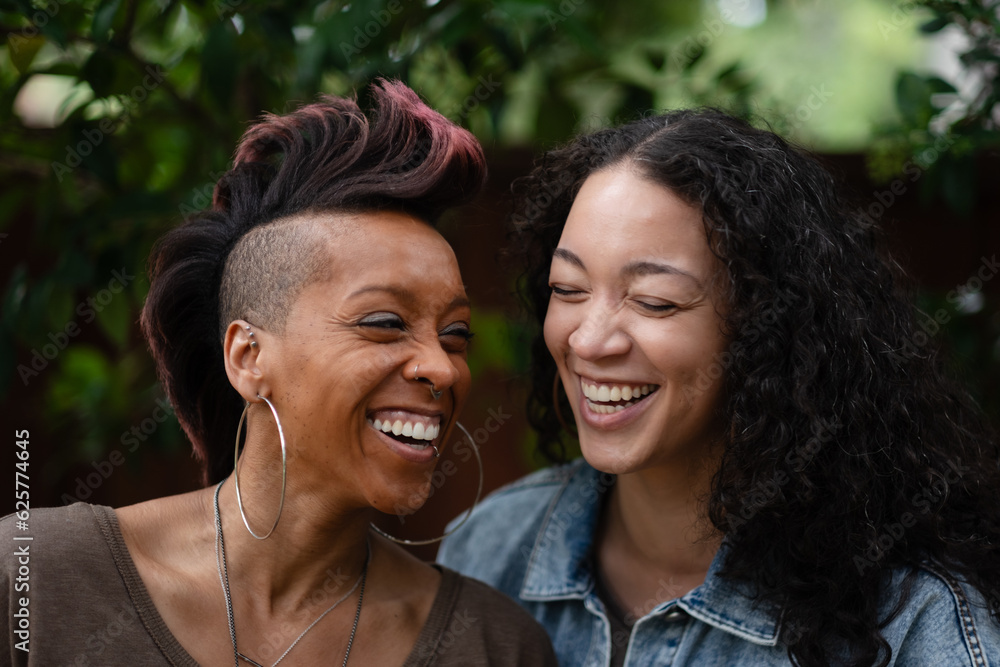 Naklejka premium A candid, real moment of a lesbian couple embracing each other and laughing. They are celebrating their engagement with a happy, joyful photo shoot. Adding backstory, they are a multiracial couple.