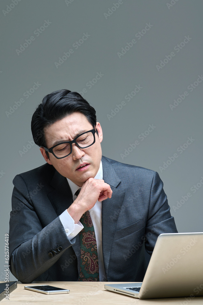 A middle-aged office worker in a suit sits at his desk and expresses various emotions using his smartphone, glasses, and laptop. A middle-aged office worker in a suit sits at his desk and expresses various emotions using his smartphone, glasses, and laptop.
