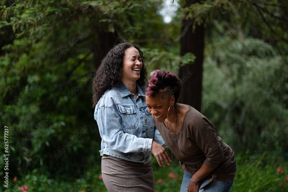 Two women express a real-life, candid moment of joyous laughter as they have fun together in a forested area. Adding backstory, they are a lesbian couple celebrating their engagement. Two women express a real-life, candid moment of joyous laughter as they have fun together in a forested area. Adding backstory, they are a lesbian couple celebrating their engagement.