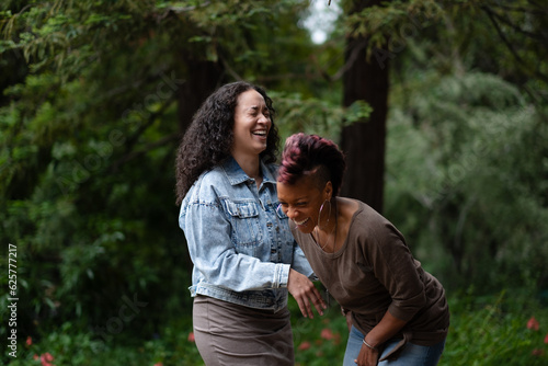 Two women express a real-life, candid moment of joyous laughter as they have fun together in a forested area. Adding backstory, they are a lesbian couple celebrating their engagement. 