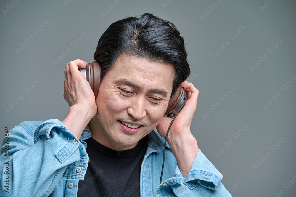 Middle-aged man sitting in a chair, wearing a headset and listening to music on his smartphone Middle-aged man sitting in a chair, wearing a headset and listening to music on his smartphone