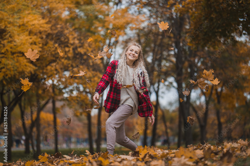 middle aged woman plays with autumn leaves. Mature blonde woman in a plaid shirt with a bouquet of yellow leaves in the park in autumn enjoys life, walks and throws leaves