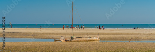 Coastline from Morondava with a baobab wood boat at low tide on sand, background with people panorama photo