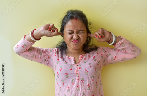 Angry annoyed young Indian woman plugging her ears to avoid loud noise, having an irritated look. Negative human emotions and reaction