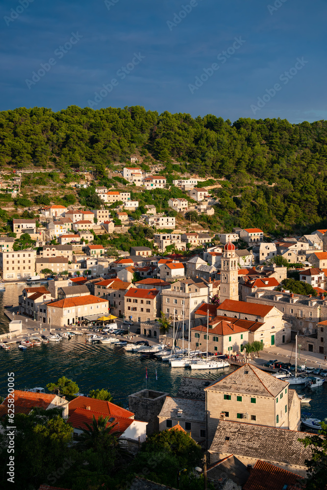 View over Pučišća village on Brac island, Croatia. Mediterranean holiday destination with picturesque harbor fjord in warm summer evening light at golden hour. Idyllic atmosphere in adriatic sea.