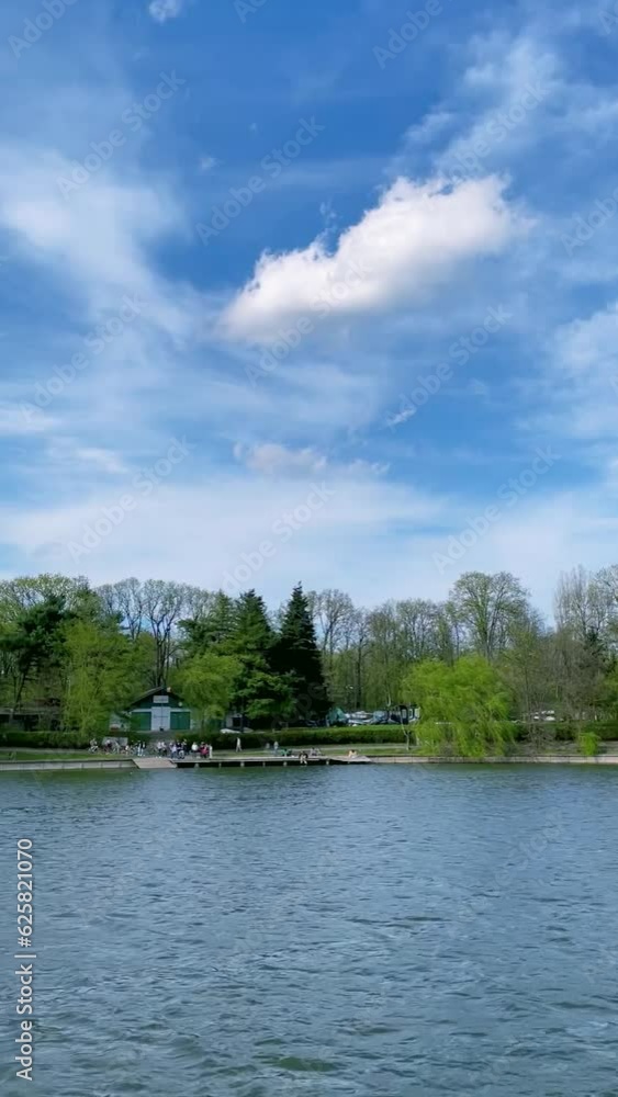 HD Video, vertical orientation -Scenic view from a tour boat on Herastrau Lake, in the Park of the same name on a beautiful sunny day, with blue sky and white fluffy clouds, in Bucharest, Romania. HD Video, vertical orientation -Scenic view from a tour boat on Herastrau Lake, in the Park of the same name on a beautiful sunny day, with blue sky and white fluffy clouds, in Bucharest, Romania.