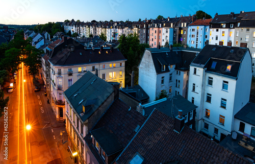 Evening panorama of Wuppertal Langerfeld Germany from historic railway bridge “Schwarzbach Viadukt“. Illuminated residential old buildings seen from above. Cityscape from “Nordbahn“ bicycle path. photo