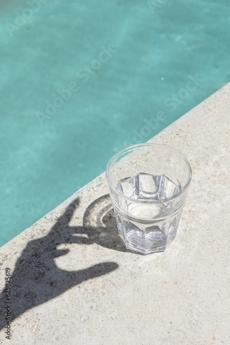 Glass of Water By the Swimming Pool with Hand Shadow During Sunny Summer Day