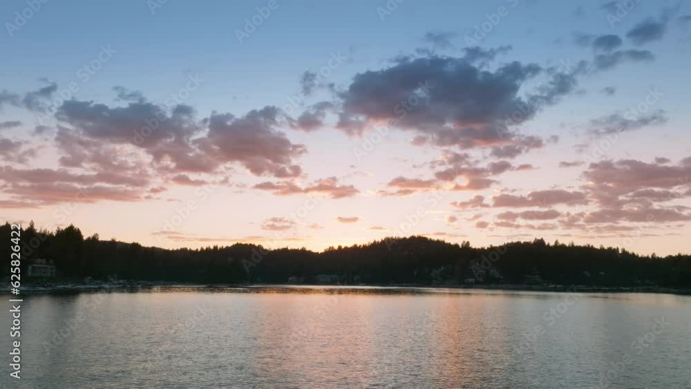 Drone flying over waterfront of Lake Arrowhead in the San Bernardino Mountains, Los Angeles, California, USA. Sunset rays reflecting on calm water surface. Colorful clouds on evening sky, 4k footage Drone flying over waterfront of Lake Arrowhead in the San Bernardino Mountains, Los Angeles, California, USA. Sunset rays reflecting on calm water surface. Colorful clouds on evening sky, 4k footage