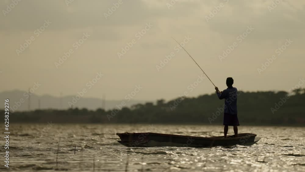 Silhouette of fishermen alone in a boat reeling up a fishing pole in a sunset lake,man recreation with fishing rod outdoor catching lifestyle fish at sunset Silhouette of fishermen alone in a boat reeling up a fishing pole in a sunset lake,man recreation with fishing rod outdoor catching lifestyle fish at sunset