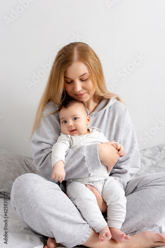 Mom and baby play on the bed. Mother and son, happy family, beautiful blonde girl and cute baby at home.