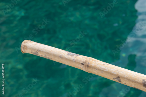 Close up shot fo a bambooo row or oar in front of a pristine, crystal clear turquoise tropical water. Exotic vacation mood. photo