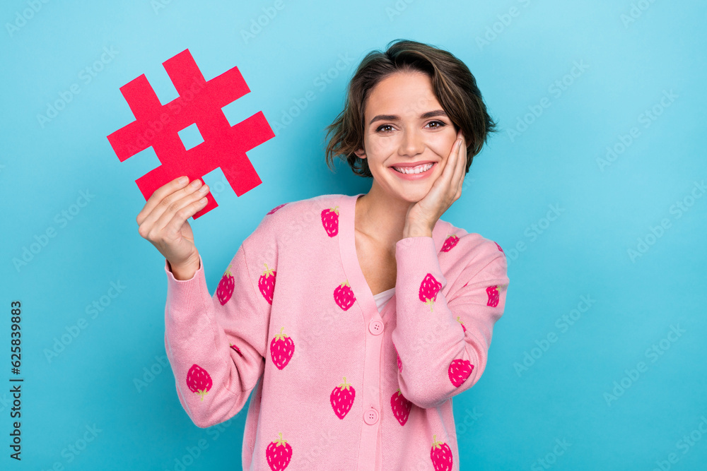 Photo of stunning positive lady toothy smile arm touch cheek hold paper hashtag symbol card isolated on blue color background Photo of stunning positive lady toothy smile arm touch cheek hold paper hashtag symbol card isolated on blue color background
